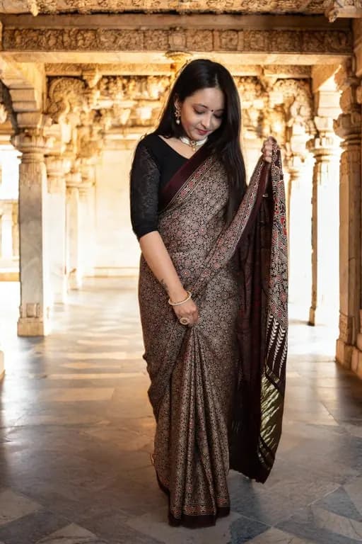 A woman holding the pallu of an Eeshani saree in a carved stone hall